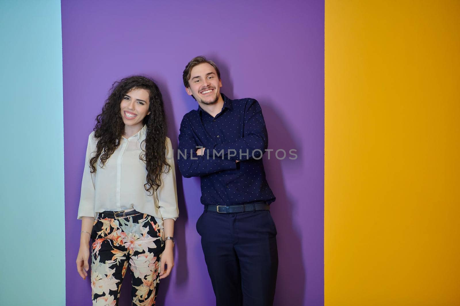 Happy young couple posing on purple background. Pretty girl with curly hair and modern fashionable clothes  standing with boy in blue shirt.