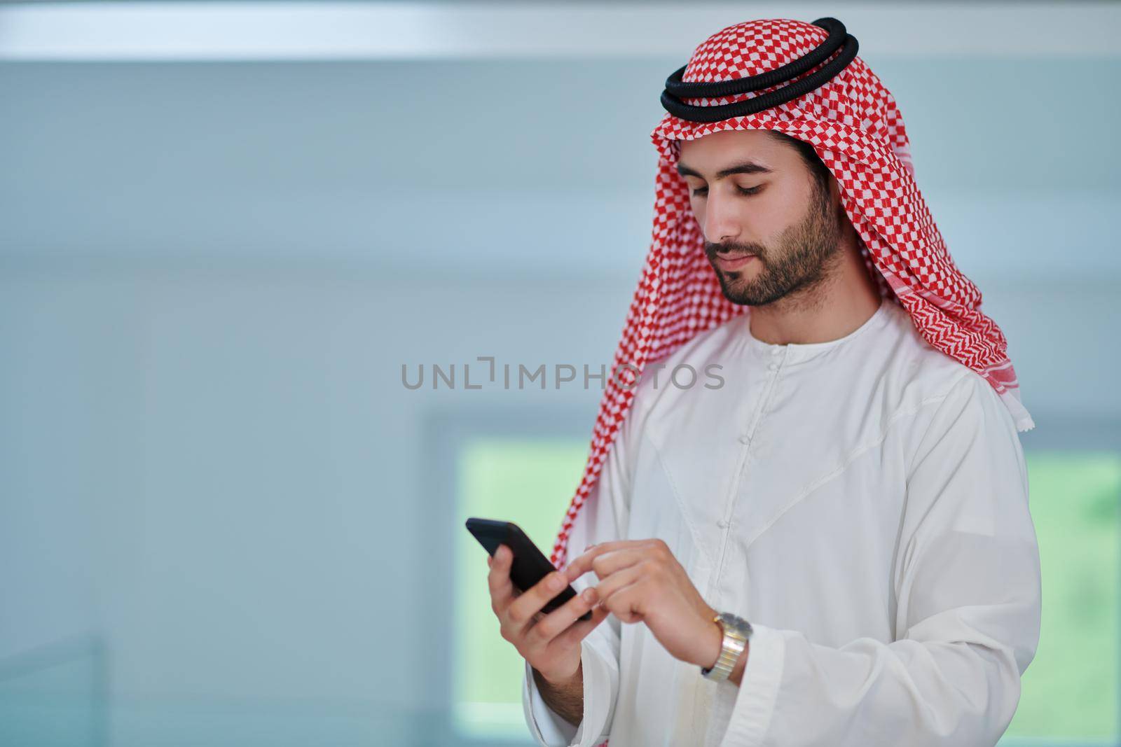 Portrait of young muslim businessman using mobile phone. Successful Arab boy in traditional clothes representing technology