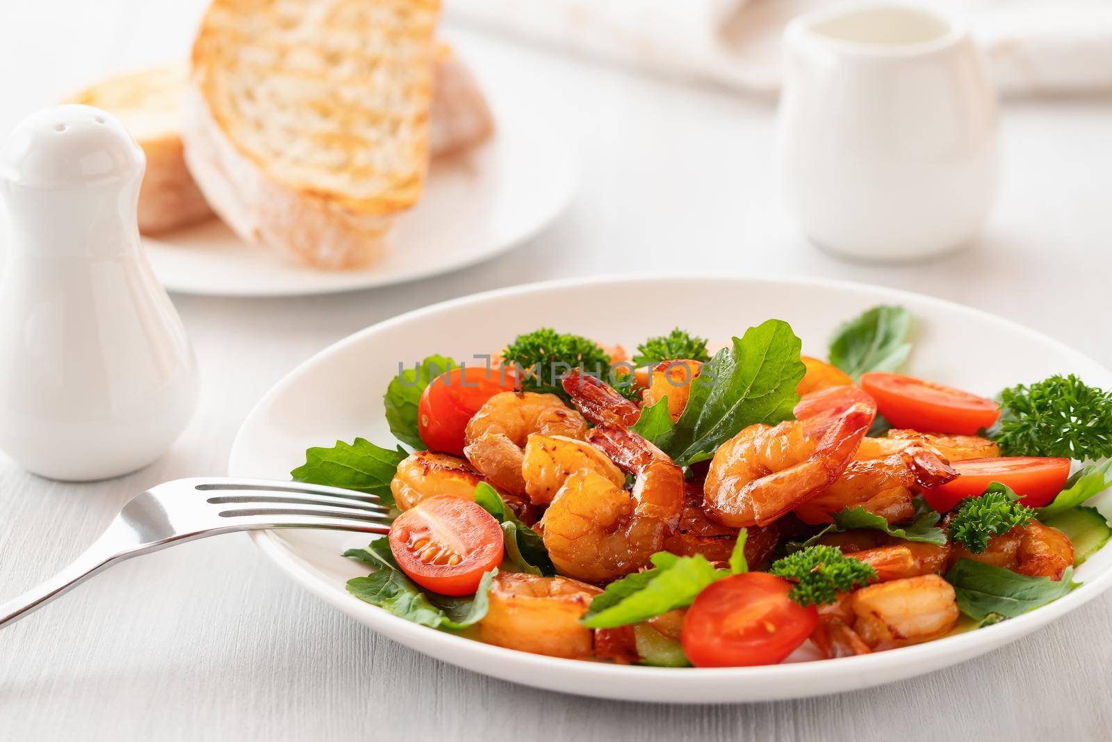 Fresh salad of shrimps, tomatoes, arugula and herbs on a white plate.