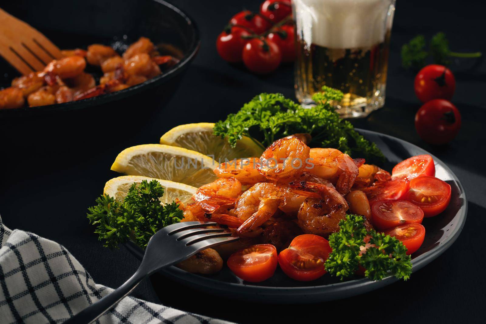 Served dinner - fried shrimp with lemon, tomatoes and herbs and beer in a glass on the table.