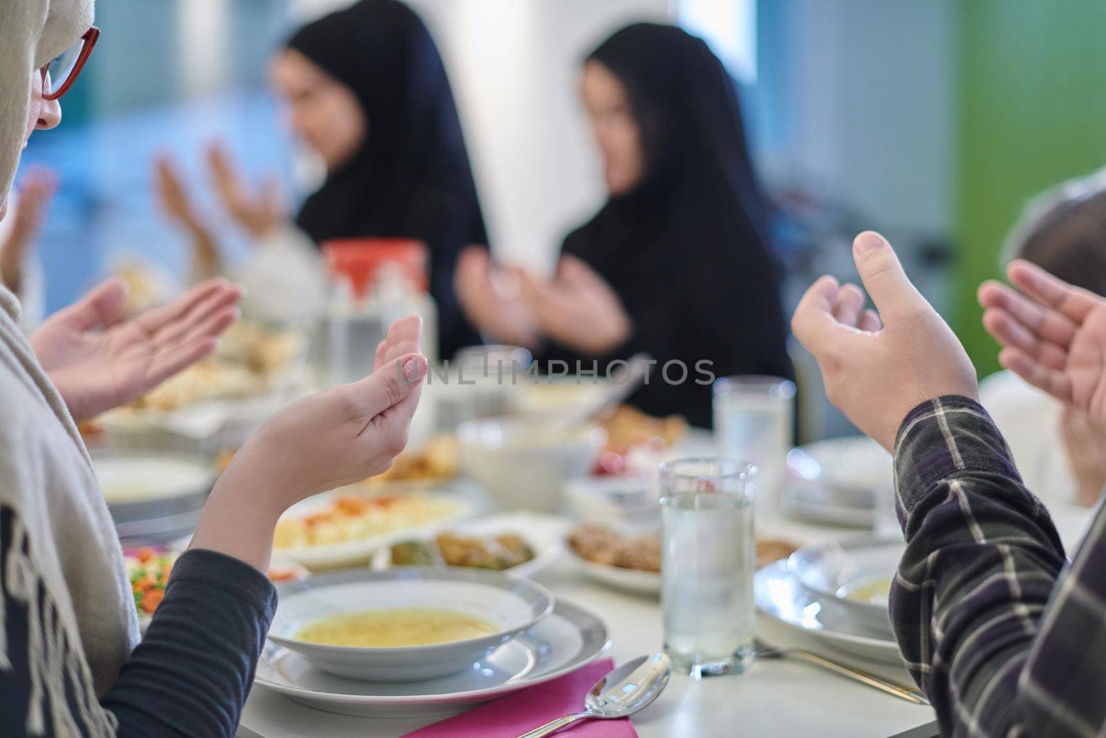 Muslim family making iftar dua to break fasting during Ramadan. Arabian people keeping hands in gesture for praying and thanking to Allah before traditional dinner