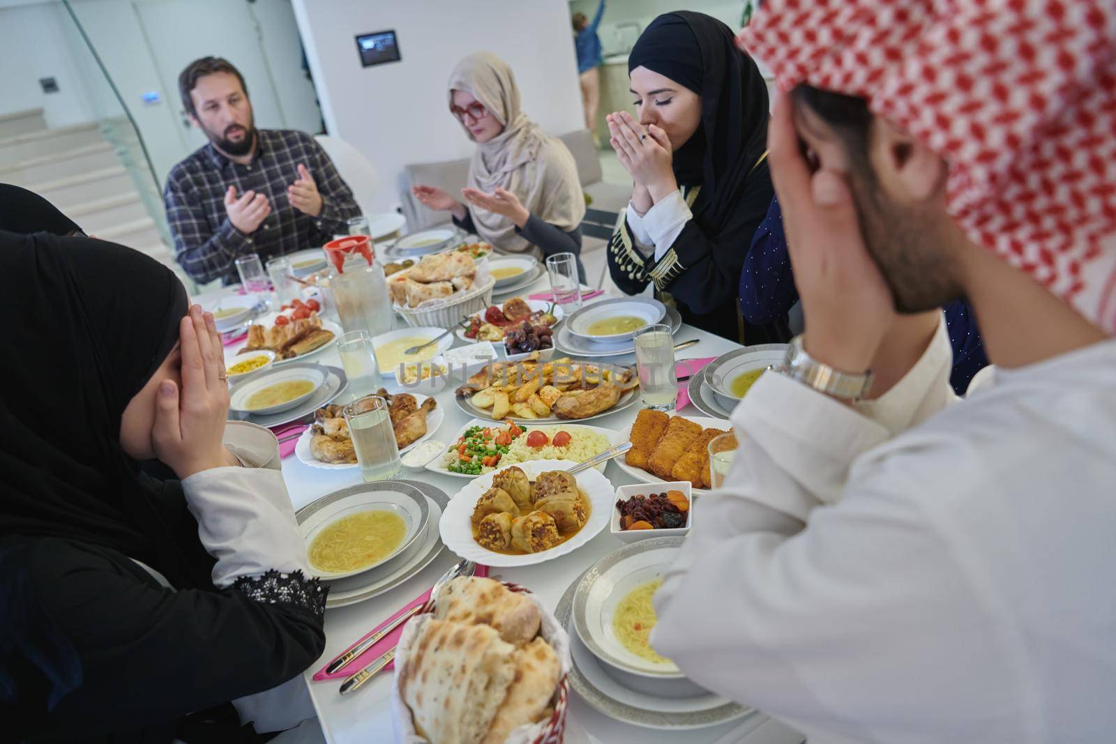 Muslim family making iftar dua to break fasting during Ramadan. Arabian people keeping hands in gesture for praying and thanking to Allah before traditional dinner