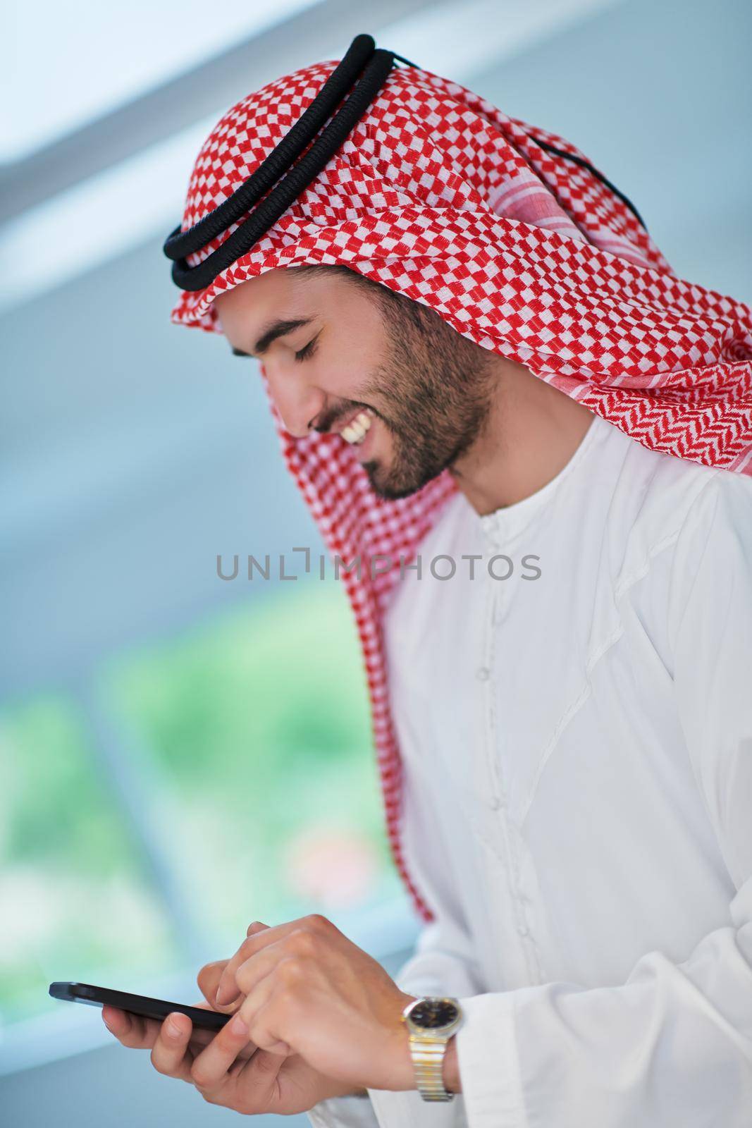 Portrait of young muslim businessman using mobile phone. Successful Arab boy in traditional clothes representing technology