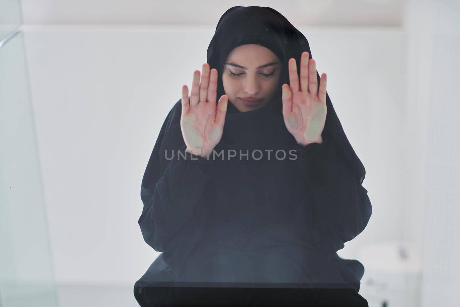 Young muslim woman doing sujud or sajdah on glass floor. Girl wearing black abaya praying salat to God during Ramadan