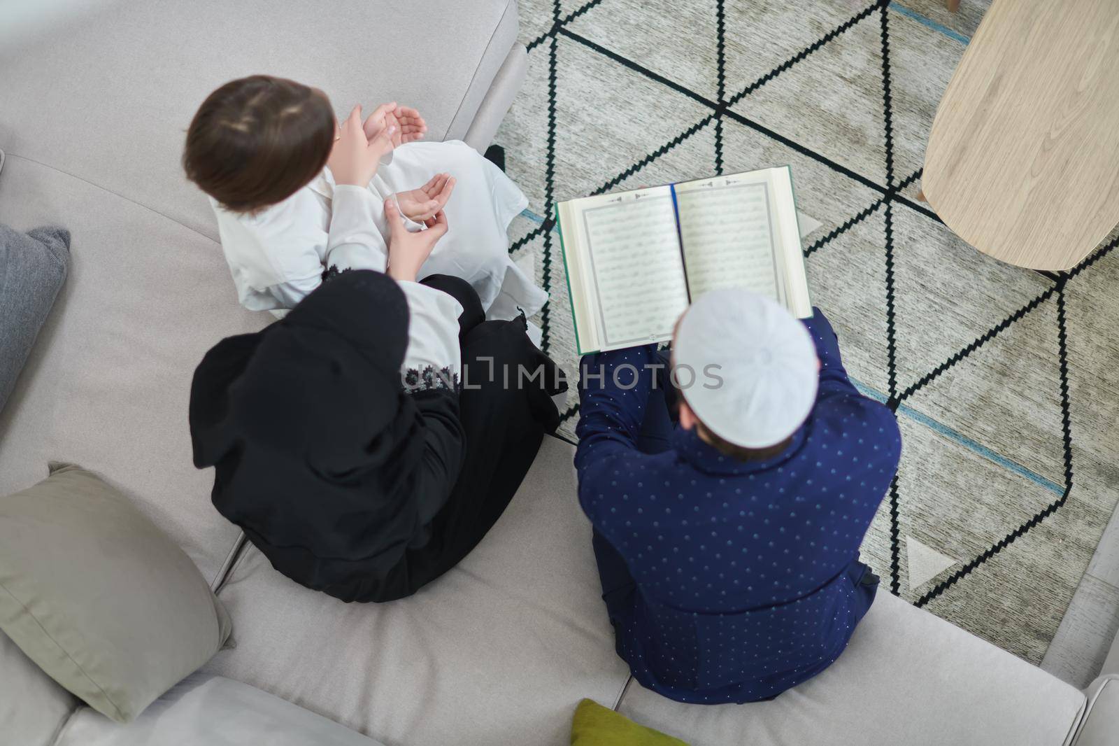 Top view of young muslim family reading Quran during Ramadan. Parents and son worshiping to God, in islamic clothes at modern home