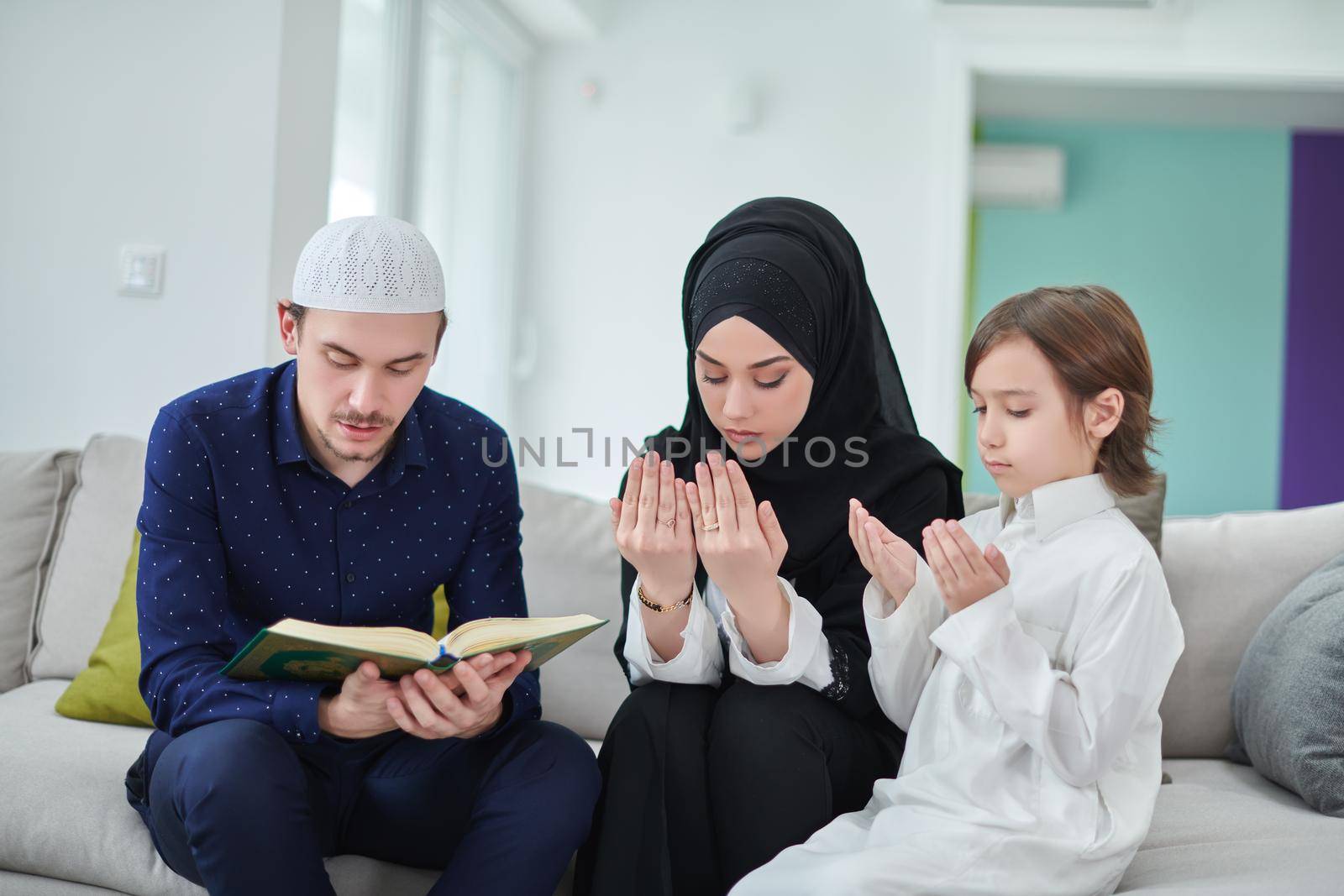 Young muslim family reading Quran during Ramadan. Parents and son worshiping to God, in islamic clothes at modern home