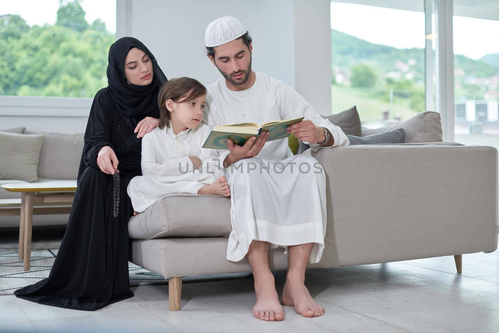 Young muslim family reading Quran during Ramadan. Parents and son worshiping to God, in islamic clothes at modern home
