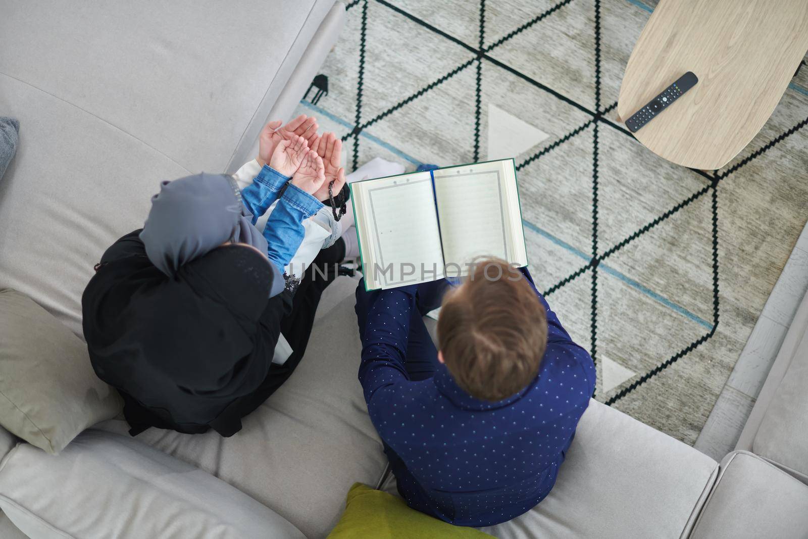 Top view of young muslim family reading Quran during Ramadan. Parents and daughter worshiping to God, in islamic clothes at modern home