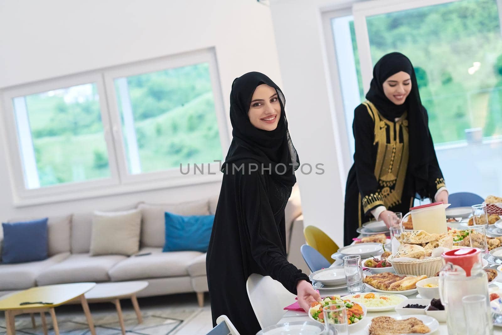 Young muslim women preparing food for iftar during Ramadan. Arabic girls in traditional abaya dresses serving table for family dinner.