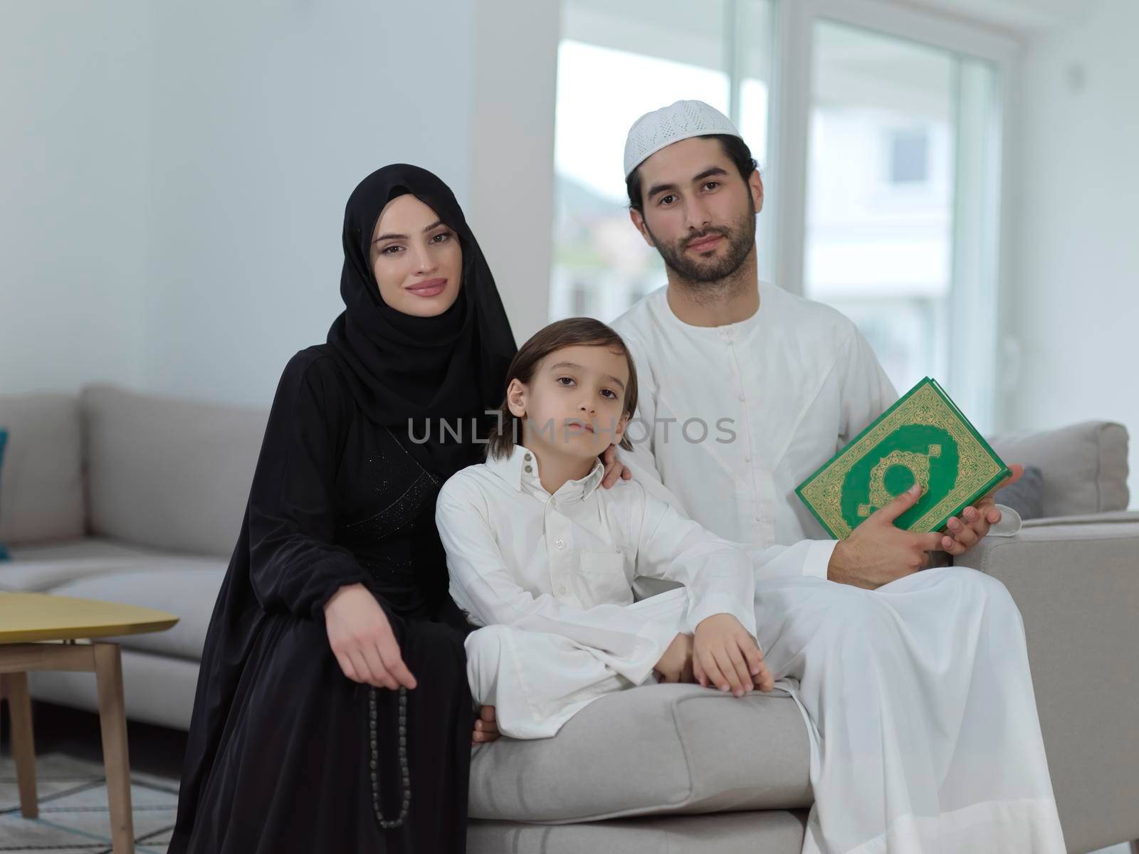 Young muslim family reading Quran during Ramadan. Parents and son worshiping to God, in islamic clothes at modern home