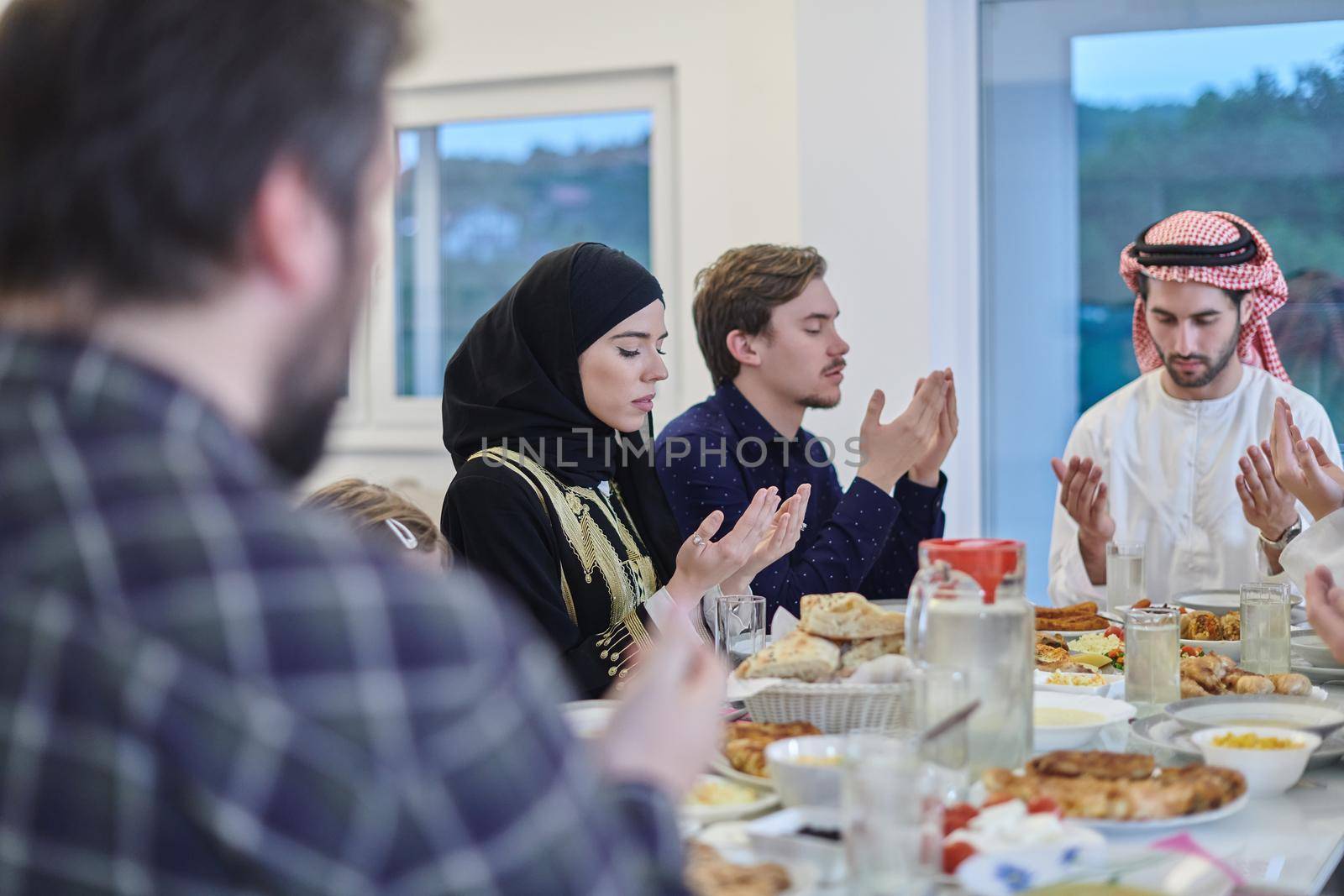 Muslim family making iftar dua to break fasting during Ramadan. Arabian people keeping hands in gesture for praying and thanking to Allah before traditional dinner