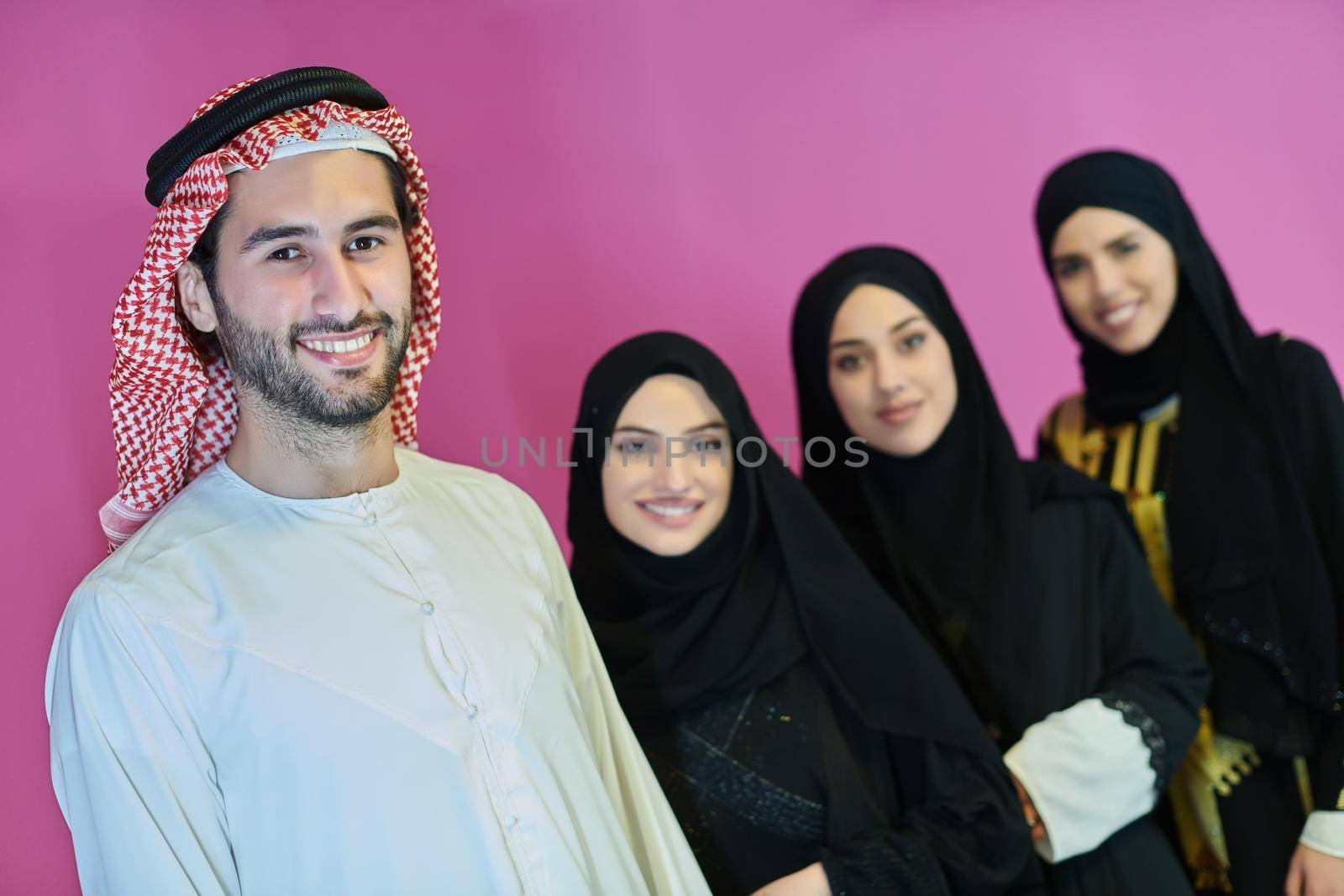 Portrait of young muslim people in traditional clothes. Happy arabic family together, man and three women isolated on pink background