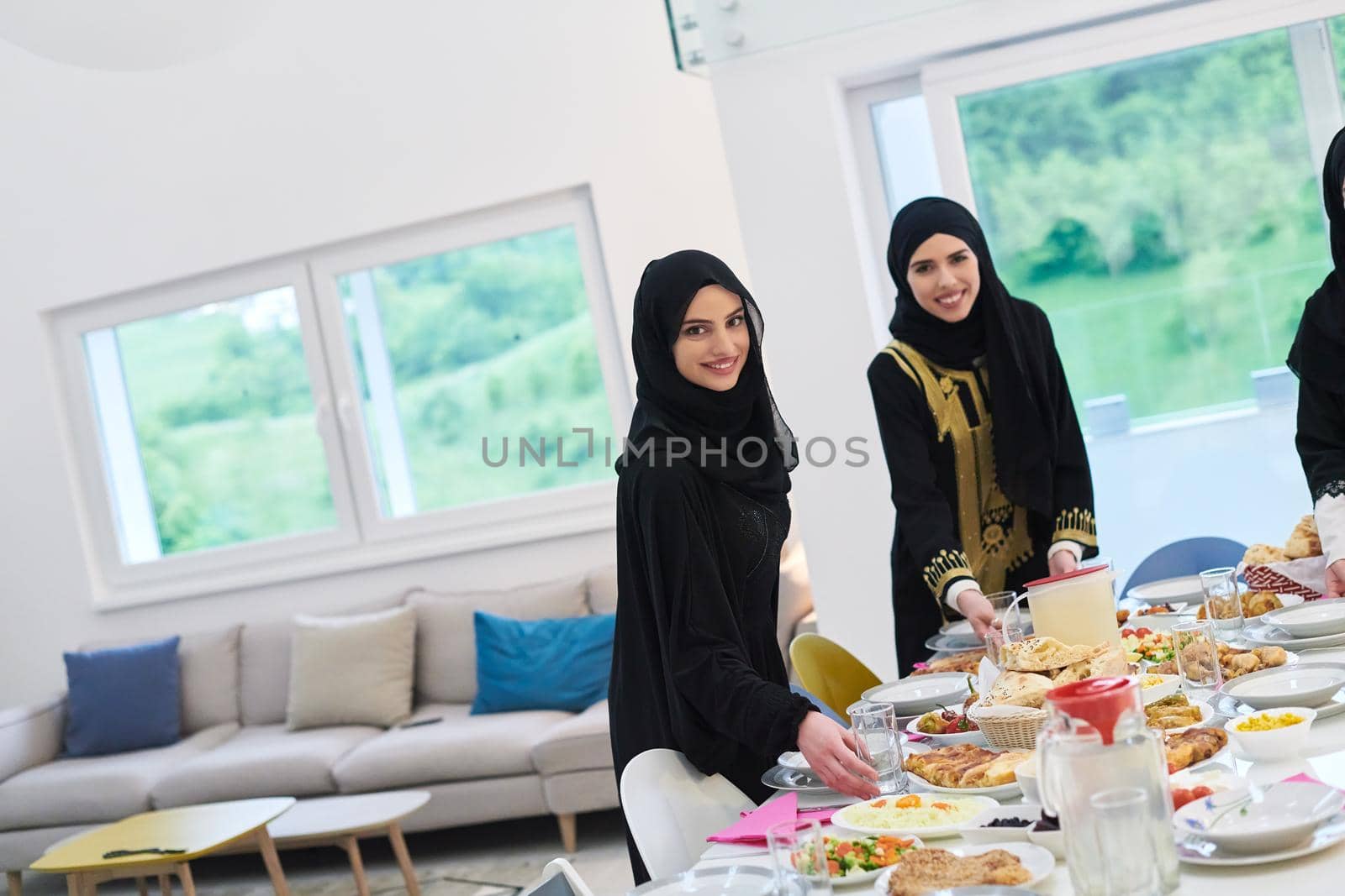 Young muslim women preparing food for iftar during Ramadan. Arabic girls in traditional abaya dresses serving table for family dinner.