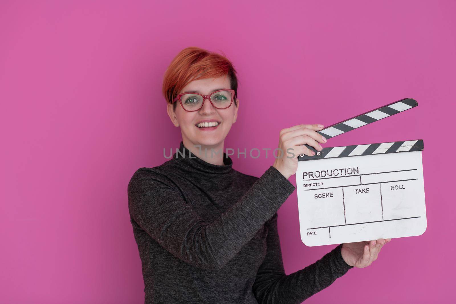 redhead woman holding movie clapper isolated against pink background  cinema concept in studio