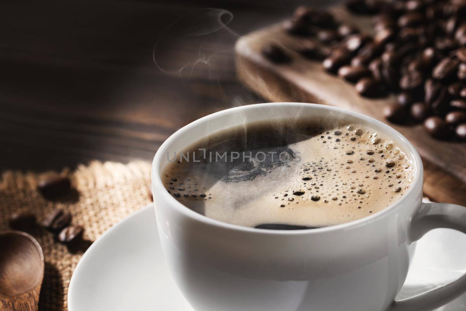 White cup of fresh hot coffee and coffee beans on wooden board on table, close up.