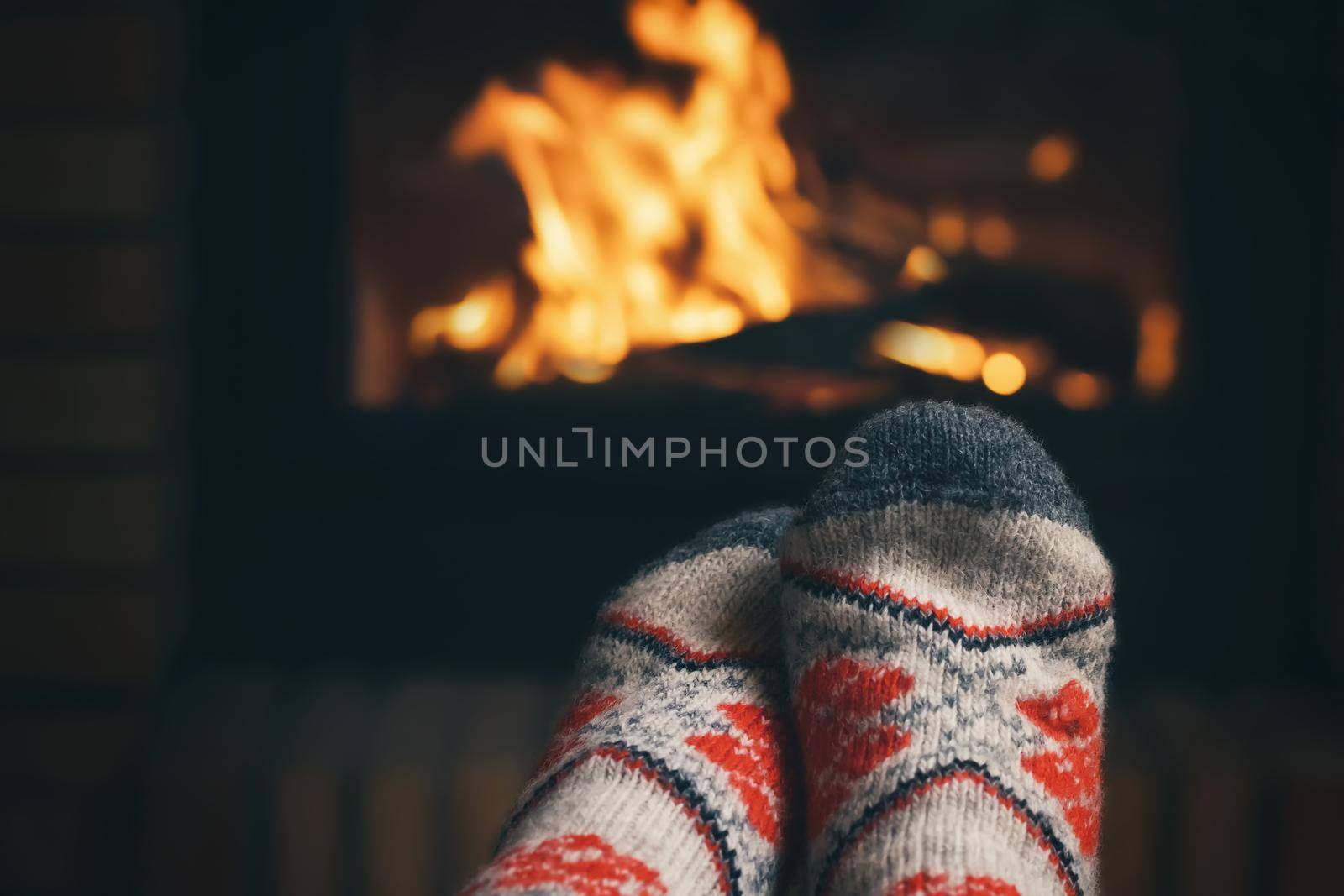 Girl resting and warming her feet by a burning fireplace in a country house on a winter evening. Selective focus