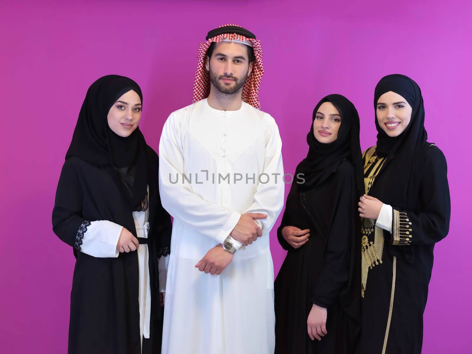 Portrait of young muslim people in traditional clothes. Happy arabic family together, man and three women isolated on pink background