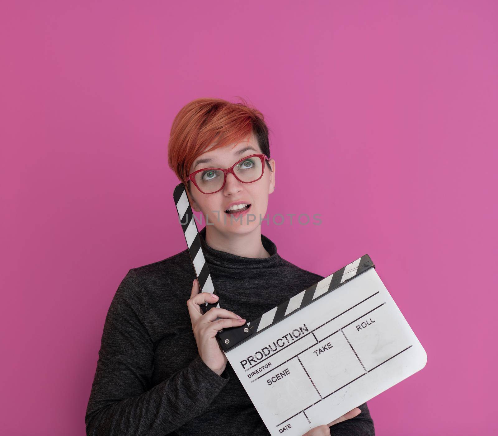 redhead woman holding movie clapper isolated against pink background  cinema concept in studio