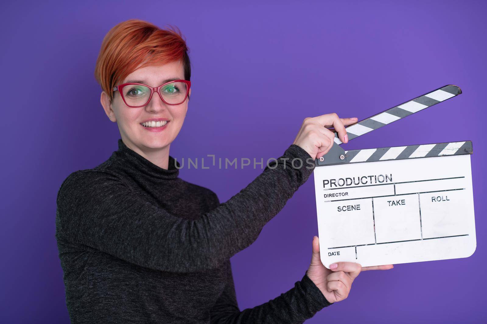 redhead woman holding movie clapper against purple  background  cinema concept