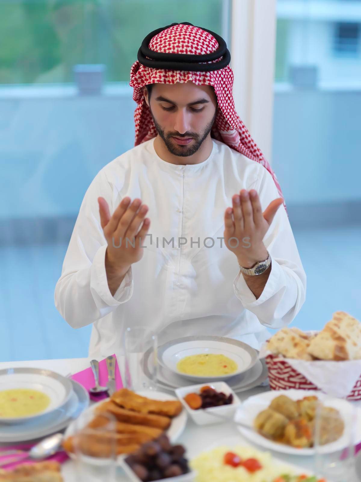 Muslim man making iftar dua to break fasting during Ramadan. Arabian boy keeping hands in gesture for praying and thanking to Allah before traditional dinner