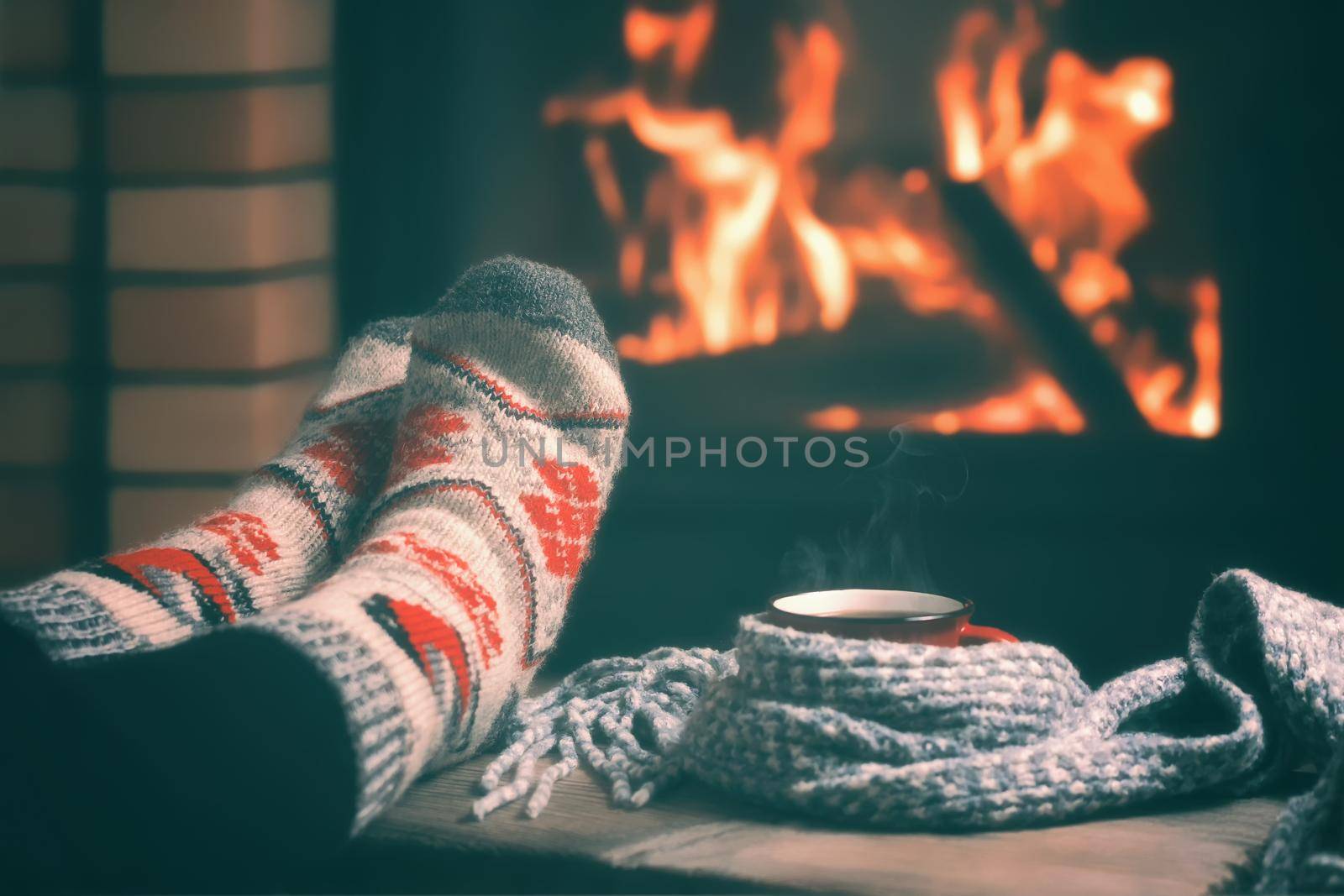 Girl resting and warming her feet by a burning fireplace in a country house on a winter evening. Selective focus. by galsand