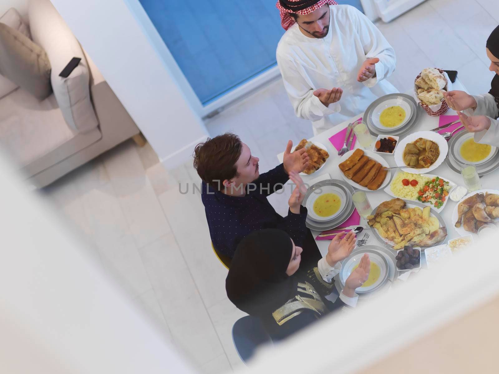 Top view of Muslim family making iftar dua to break fasting during Ramadan. Arabian people keeping hands in gesture for praying and thanking to Allah before traditional dinner