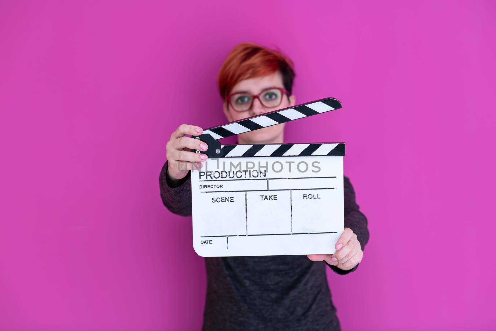 redhead woman holding movie clapper isolated against pink background cinema concept in studio