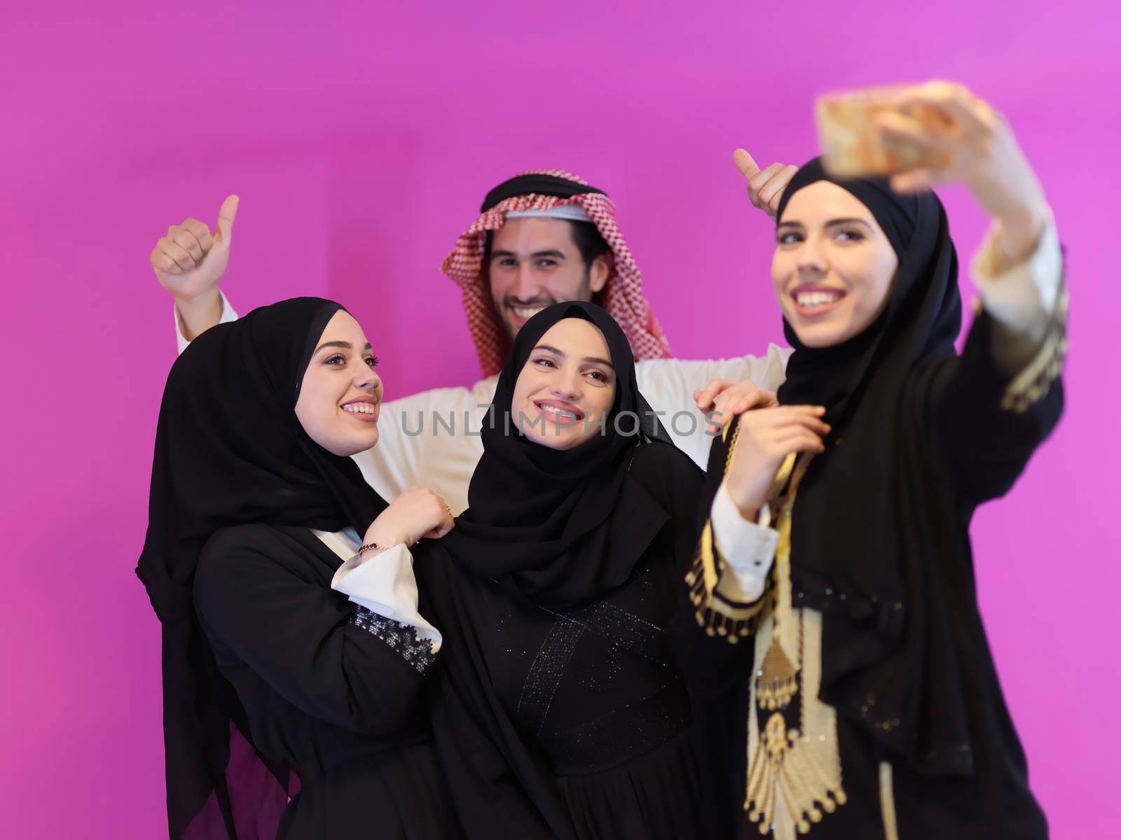 Portrait of young muslim people in traditional clothes. Happy arabic family together, man and three women isolated on pink background