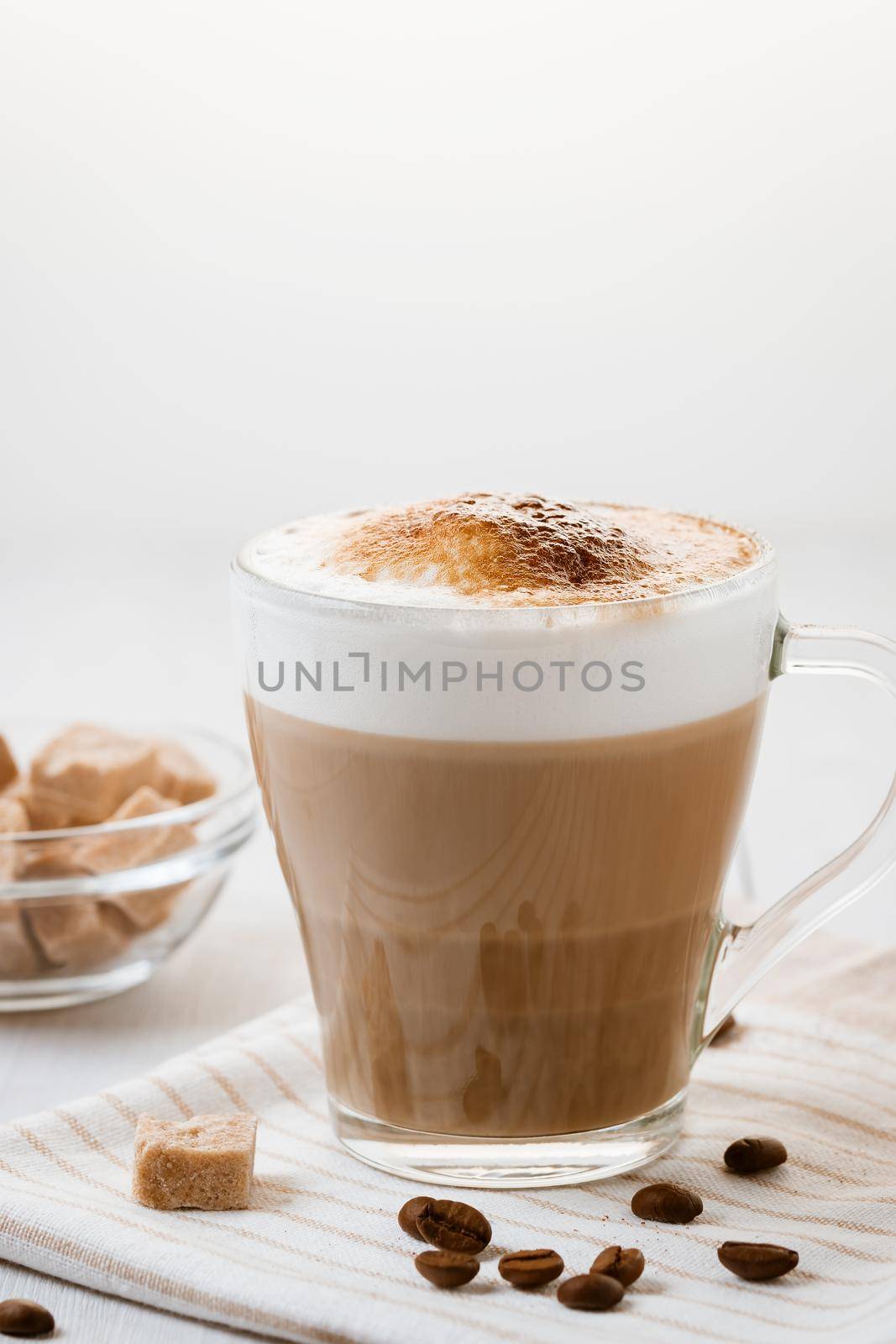 Latte coffee poured in layers with froth and a crispy chocolate top on a light kitchen table. Vertical image with copy space by galsand