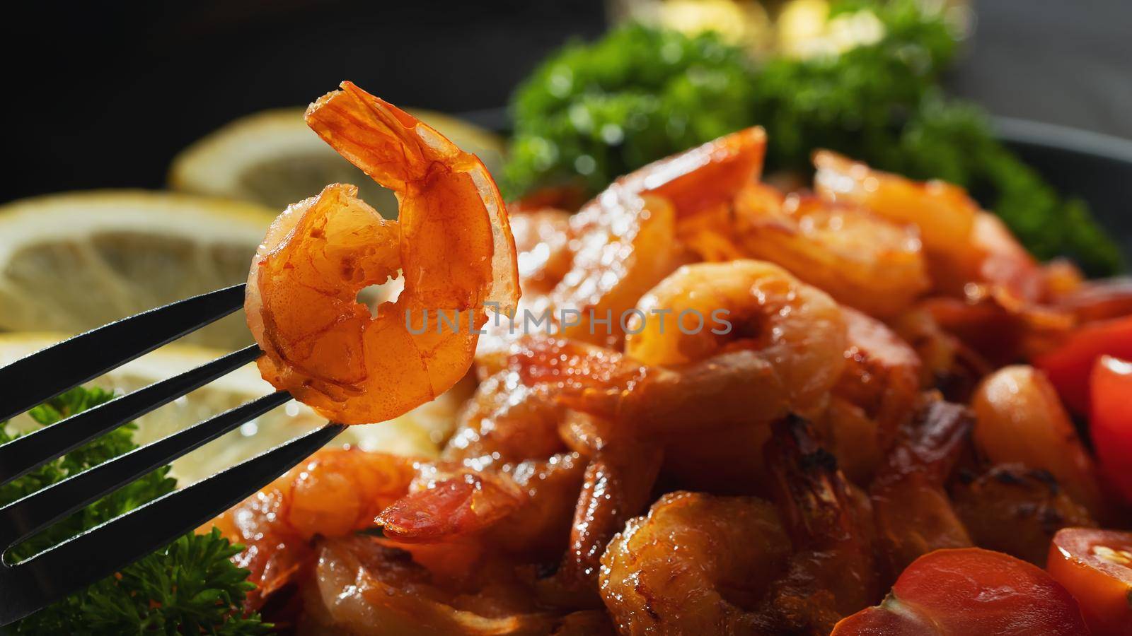 Fried shrimp on a fork close-up on a background of shrimp and greens on a plate.