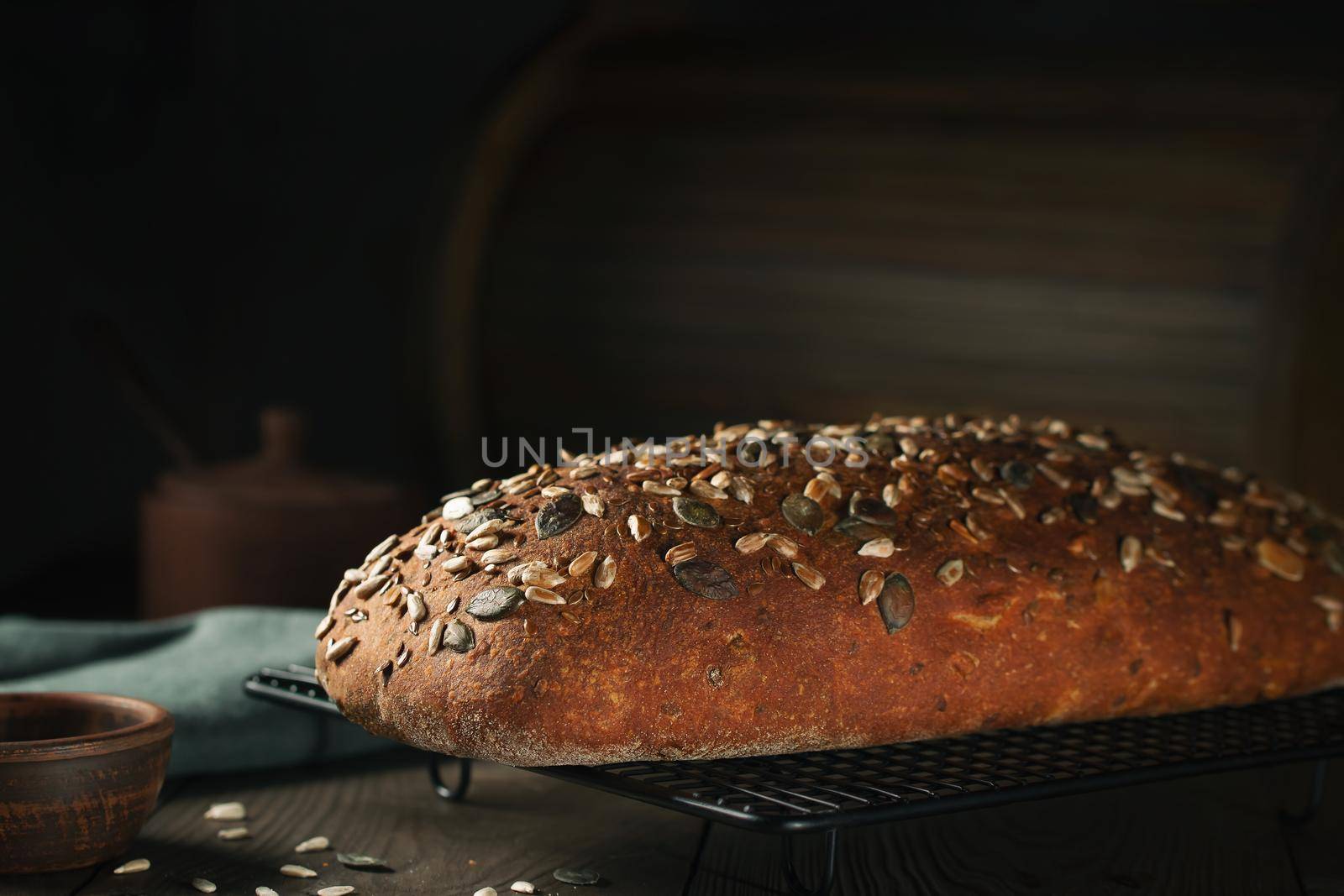 Loaf of homemade whole grain bread with seeds cool down on a wire rack on a wooden table.