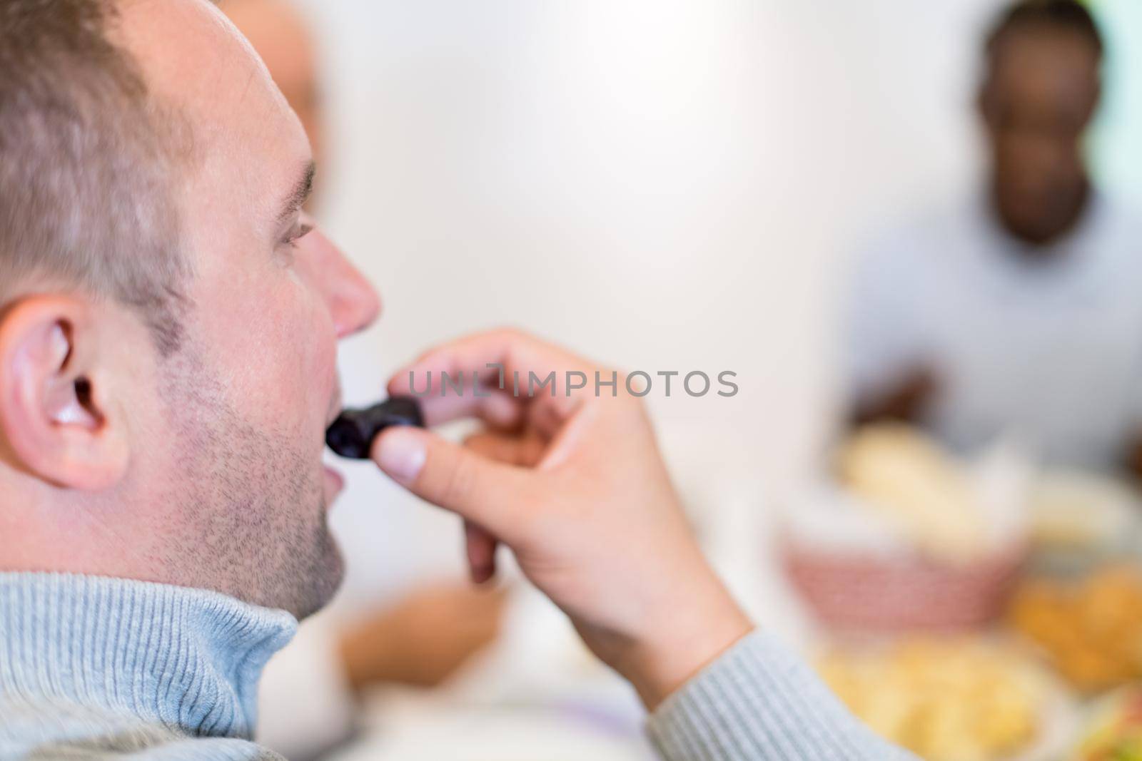 young man eating dates with modern multiethnic muslim family while enjoying iftar dinner together during a ramadan feast at home