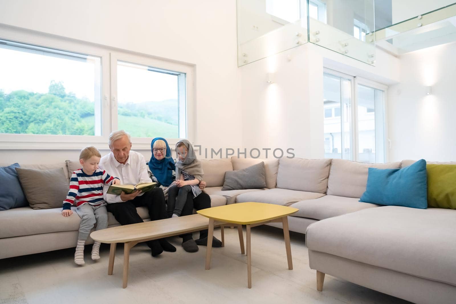 modern muslim family grandparents with grandchildren reading Quran and praying together on the sofa before iftar dinner during a ramadan feast at home