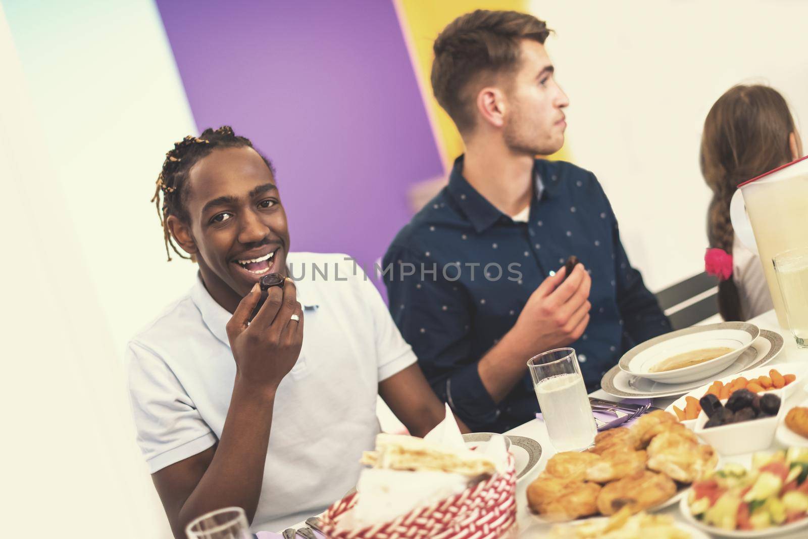 young african american man eating dates with modern multiethnic muslim family while enjoying iftar dinner together during a ramadan feast at home