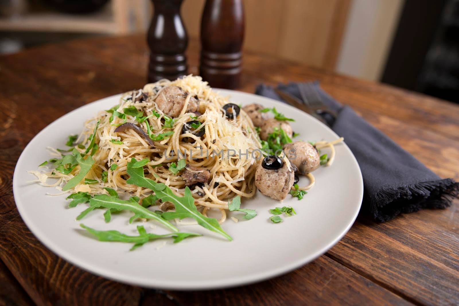 Spaghetti with meatballs, olives and arugula on wood table by Jyliana