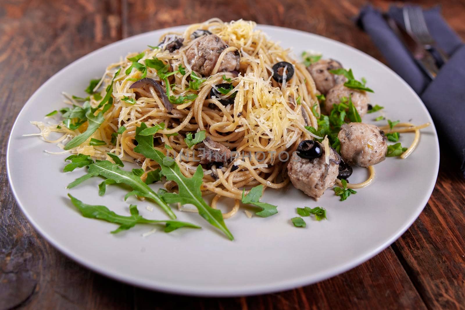 Spaghetti with meatballs, olives and arugula on wood table by Jyliana