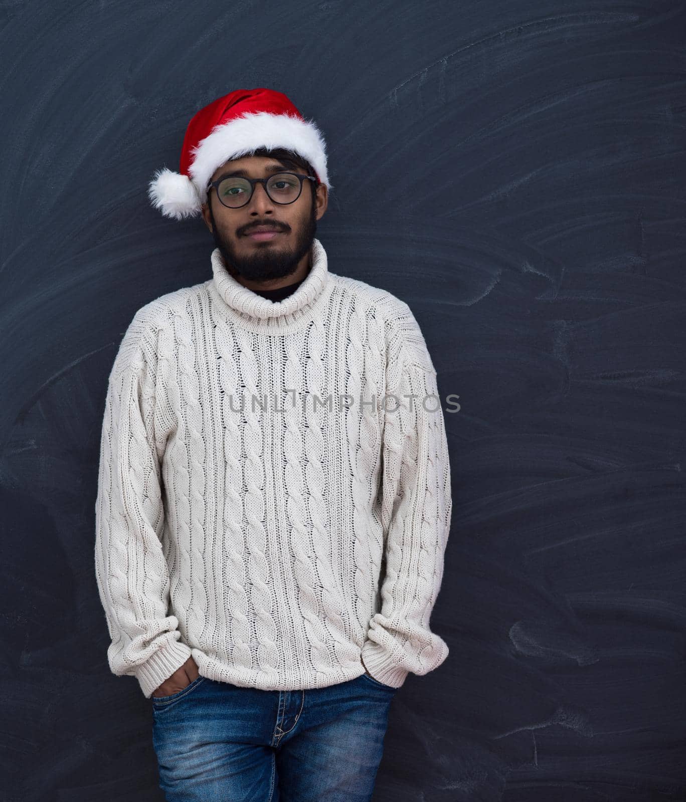 Indian man wearing traditional Santa Claus hat and white sweater  on chalkboard  background studio dark-skinned Christmas santa new year party
