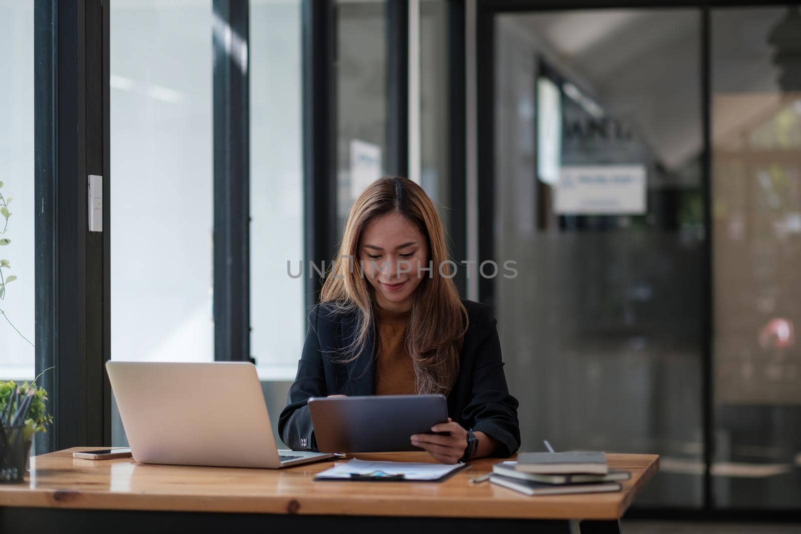Asian woman working digital tablet and laptop computer. Smiling female busy working at office.