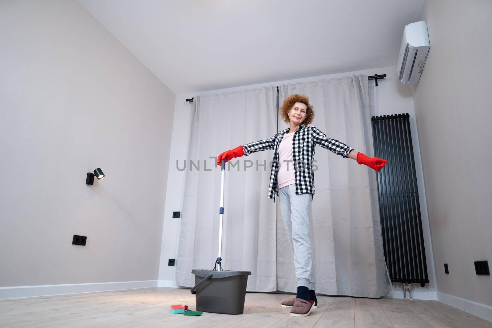 Jolly excited mature woman enjoying cleaning house, she dancing while washing floor. Happy elderly woman enjoying cleaning floors before moving to new apartment. Housework and housekeeping concept.