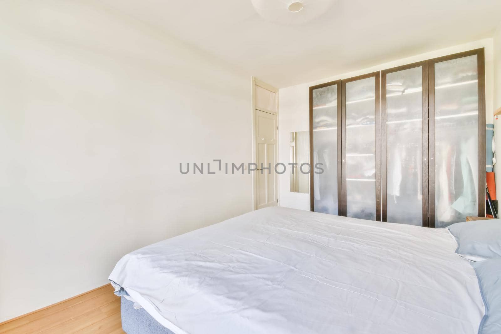 Comfortable bed covered with white blanket and located in light bedroom of modern apartment