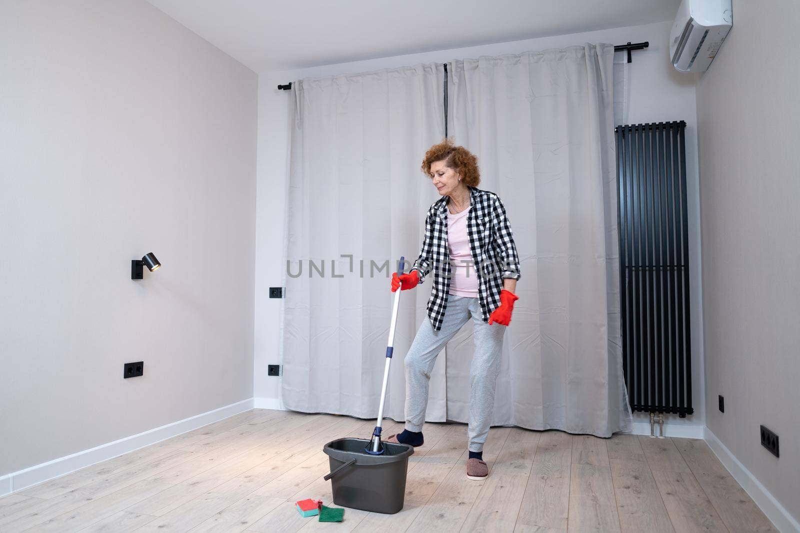 Jolly excited mature woman enjoying cleaning house, she dancing while washing floor. Happy elderly woman enjoying cleaning floors before moving to new apartment. Housework and housekeeping concept by Tomashevska