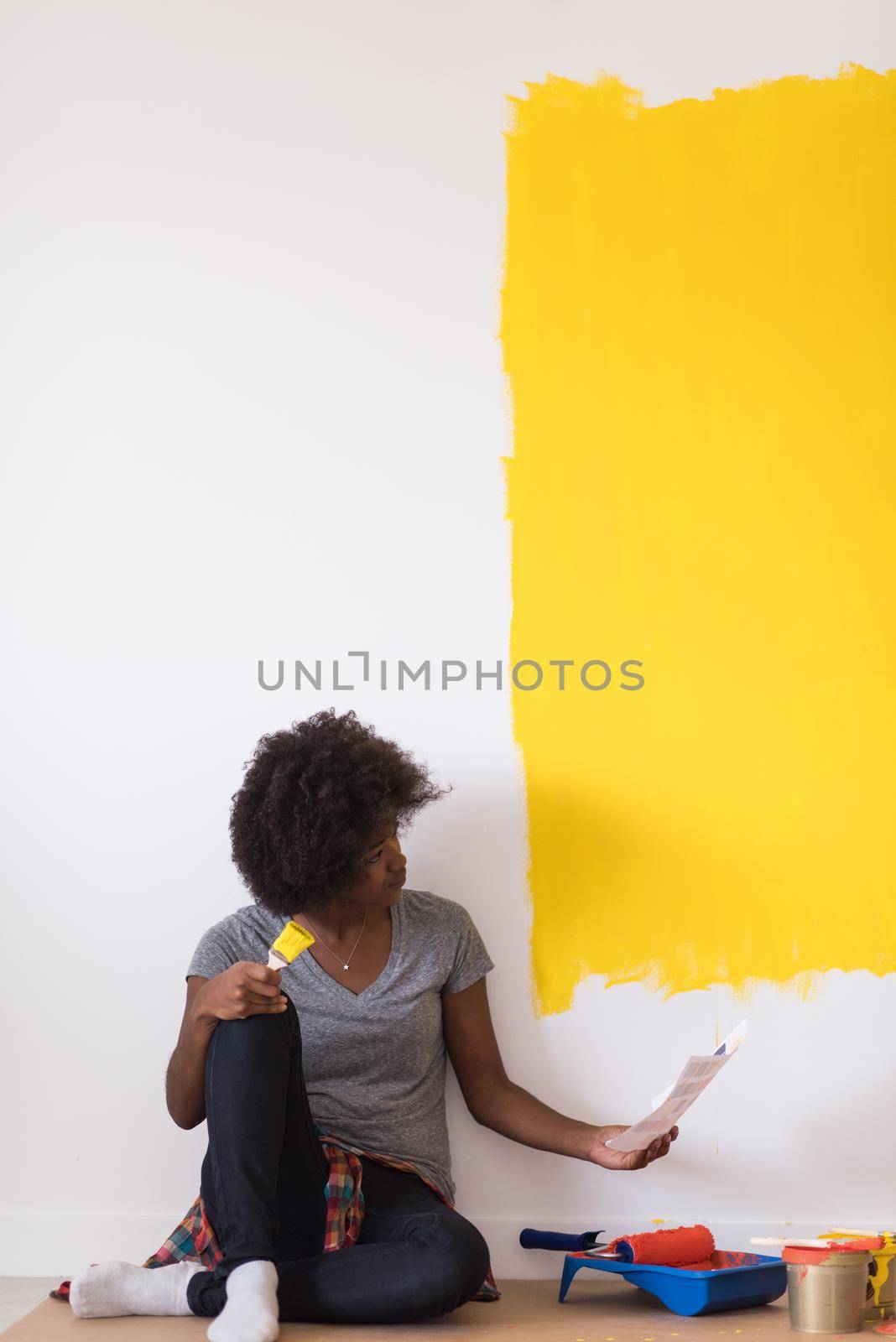 Portrait of a beautiful african american female painter sitting on floor near wall after painting.