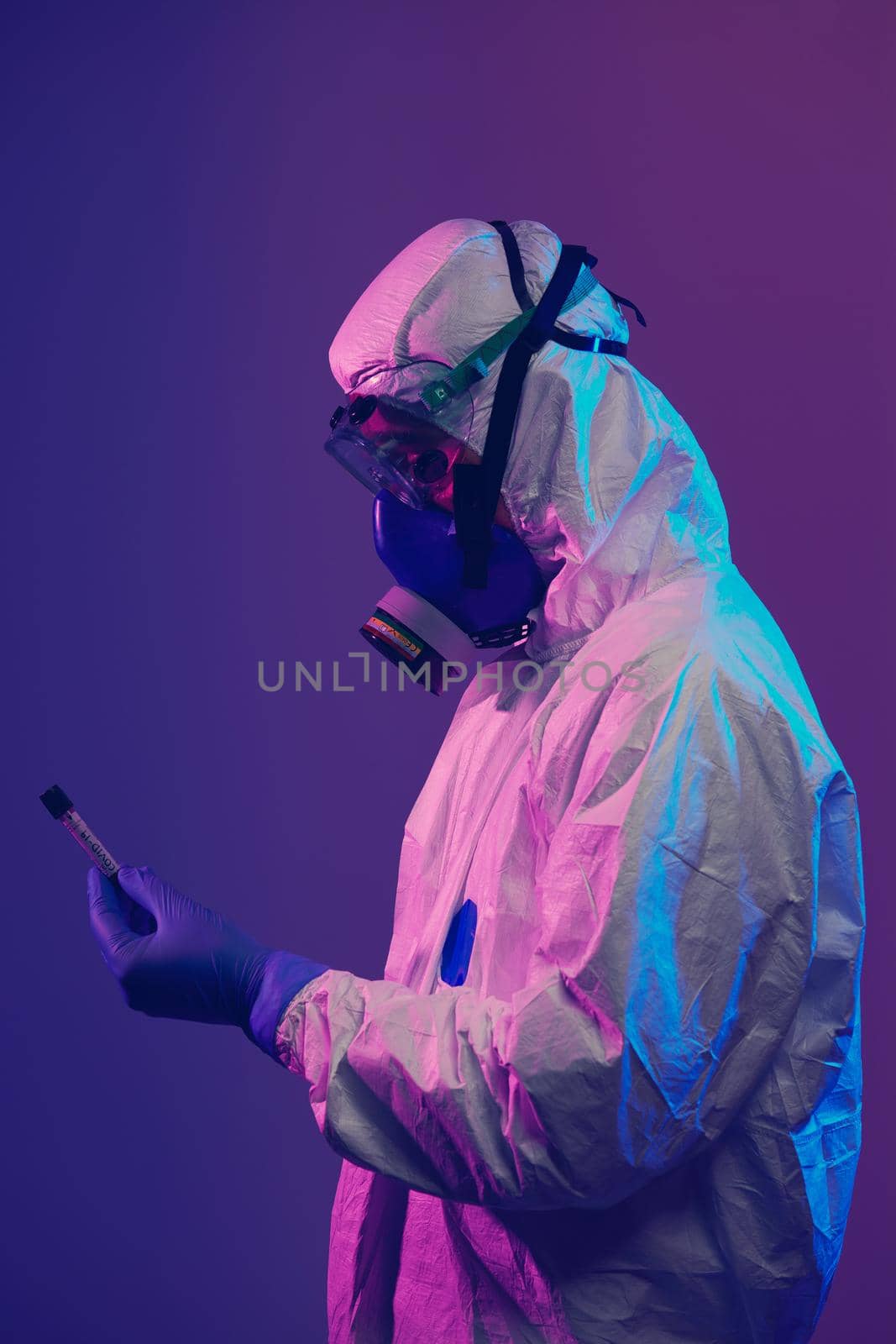 Coronavirus, Doctor holding positive covid-19 virus Blood Sample test tube. Wearing biohazard epidemic Protective mask, suit and glows neon light background