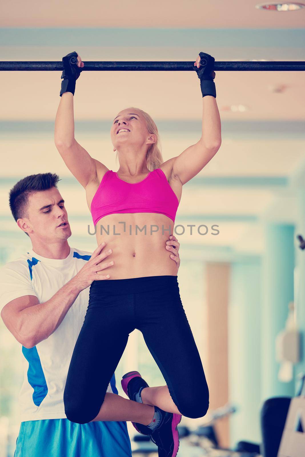 trainer support young woman while lifting on bar in fitness gym by dotshock