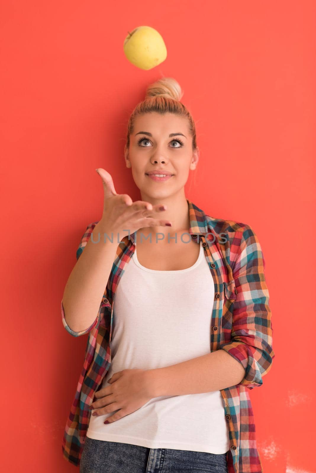 beautiful  young woman with hair bun plays with apple over color background with copyspace expressing different emotions