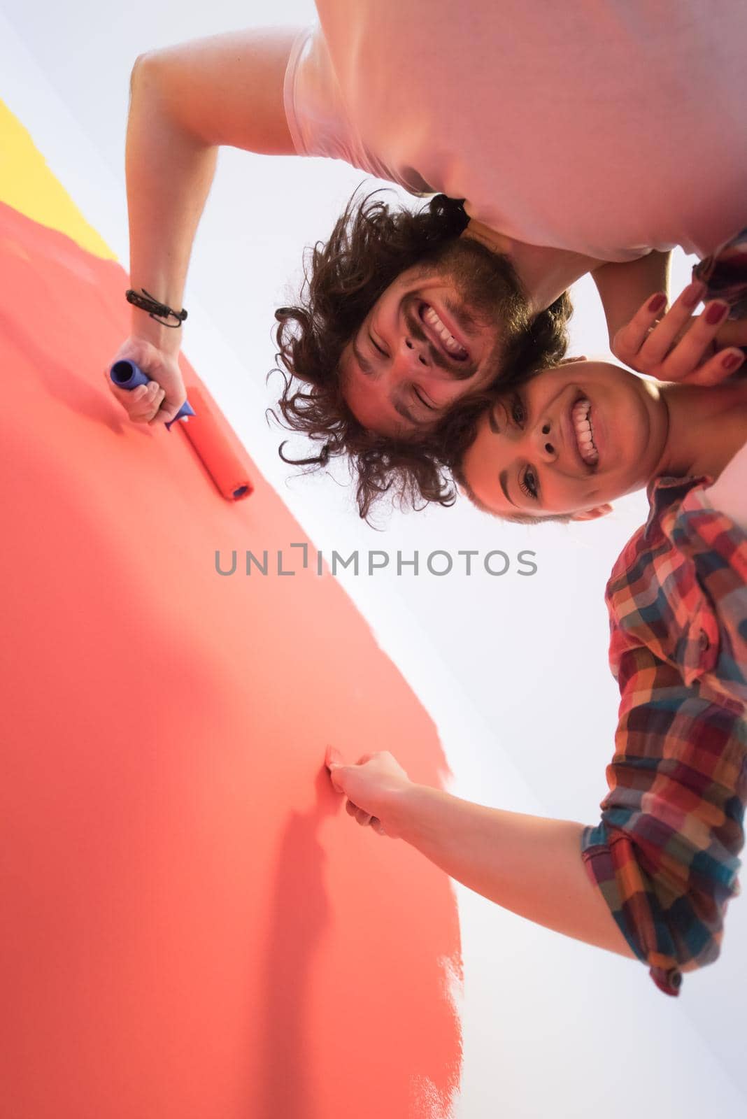 happy smiling young couple painting interior wall of new house