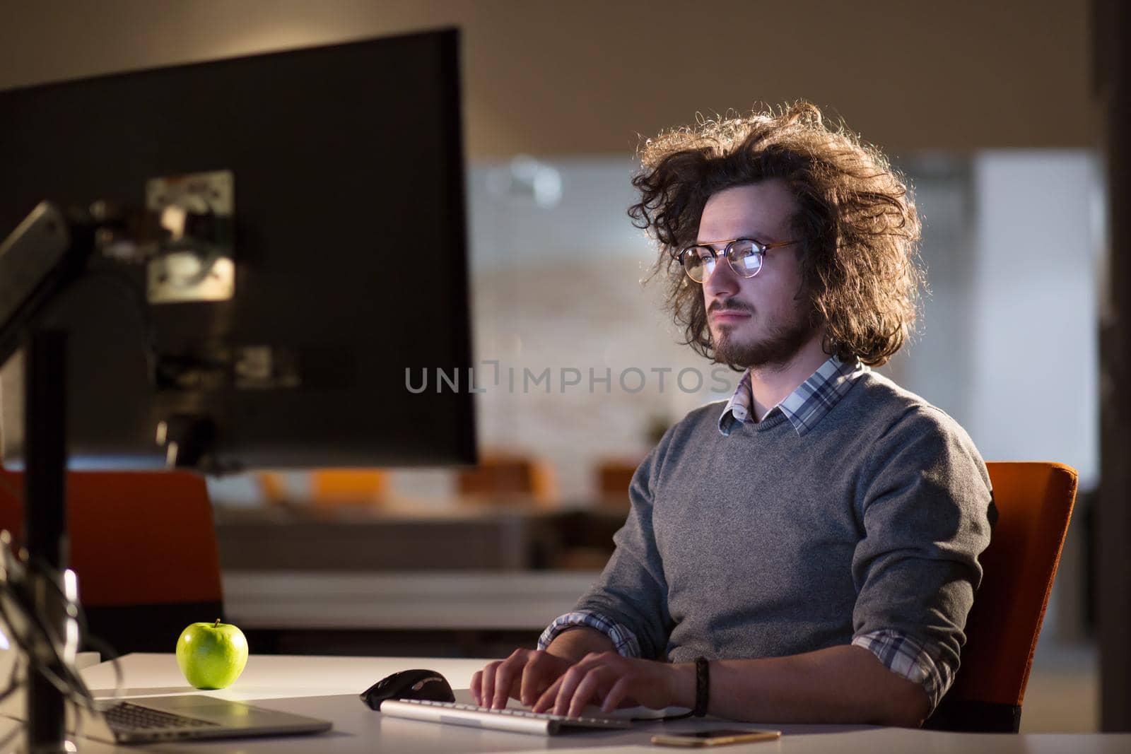 Young man working on computer at night in dark office. The designer works in the later time.