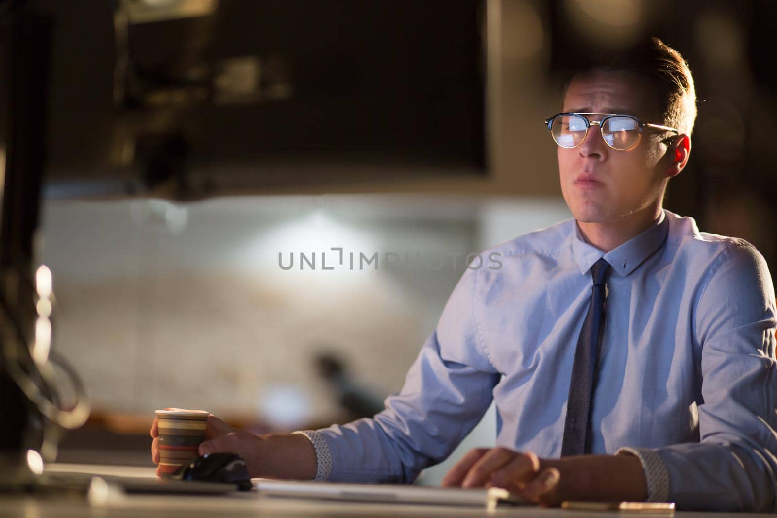 Tired businessman working late doing overtime in office at night drinking coffee to go on.