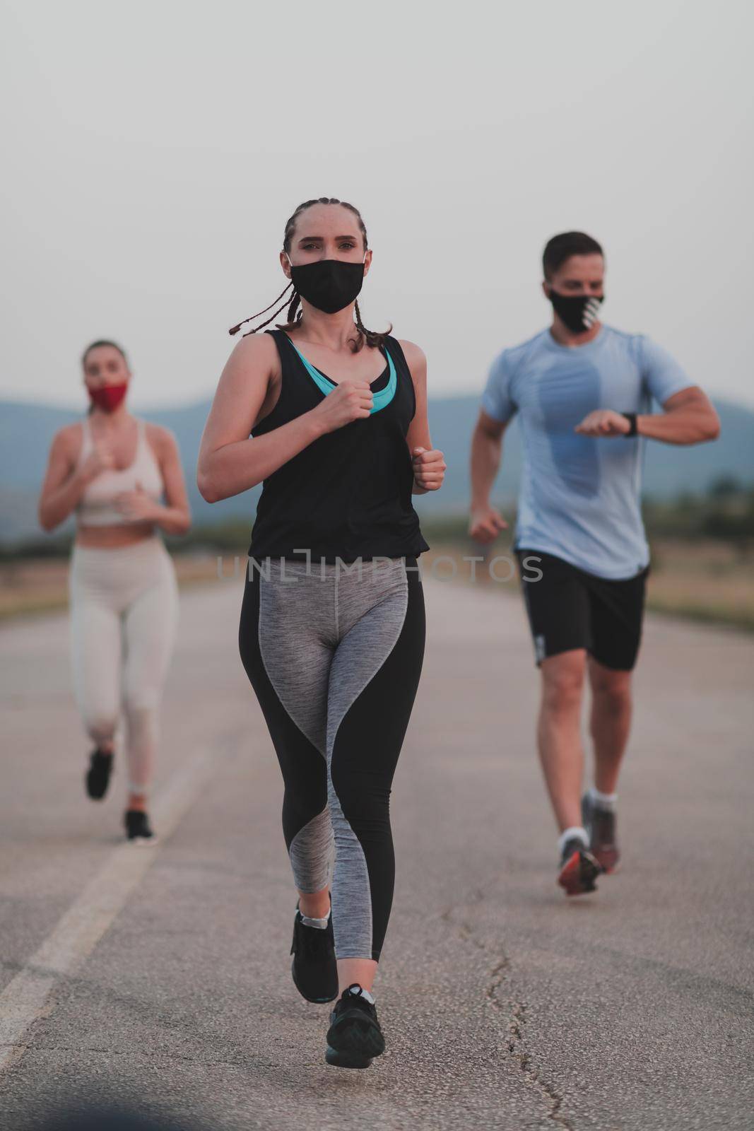 Multiethnic runners group wear face masks running keep social distance outdoor. Fit healthy diverse team wears sportswear jogging in the evening on nature sports track distancing for safety.