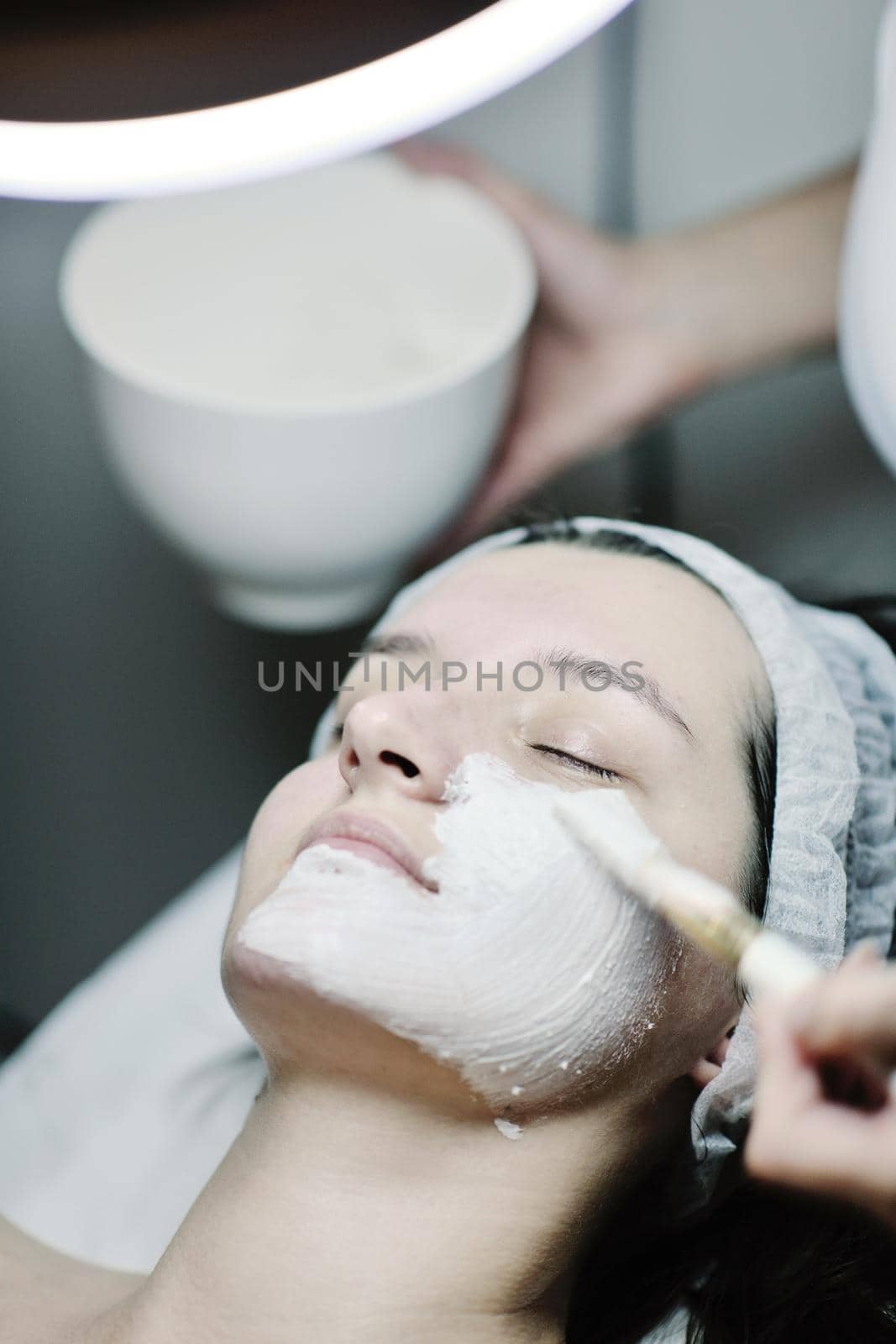 Young beautiful woman receiving cosmetic facial mask in spa beauty salon and relax